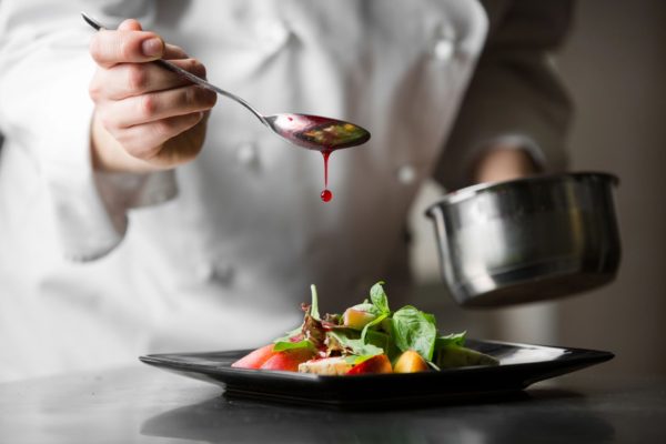 A chef pouring sauce from a spoon on food