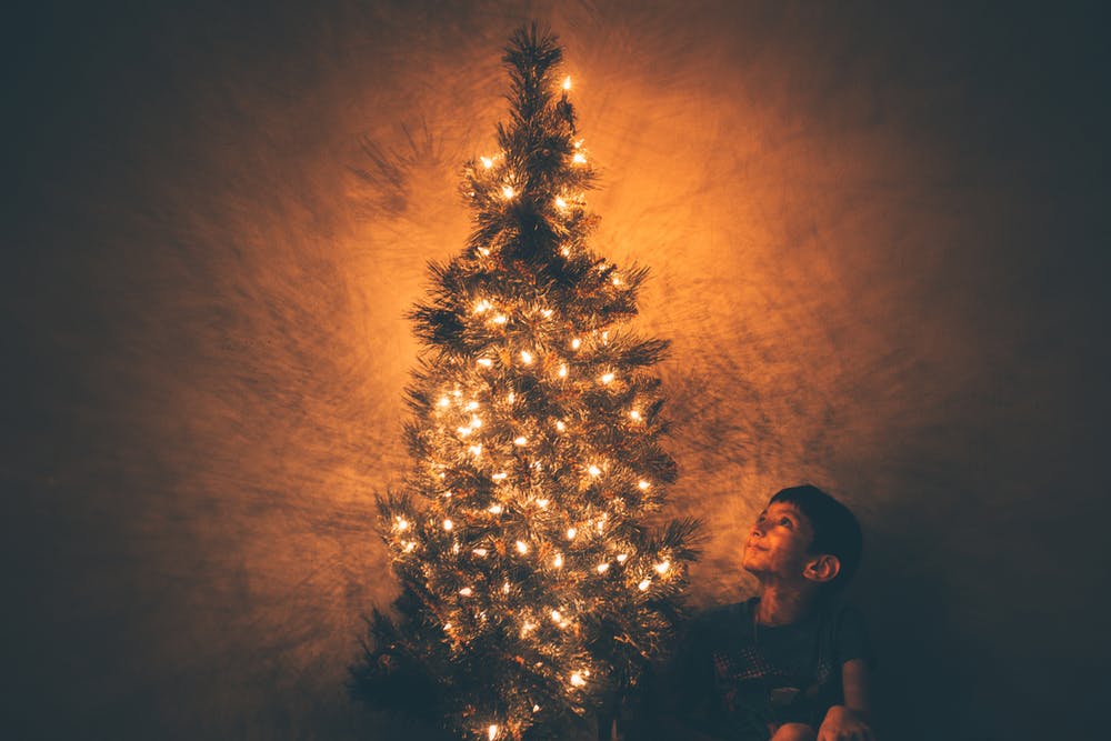 A little sitting with a lit up Christmas tree