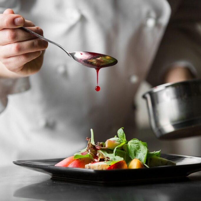 A chef pouring sauce from a spoon on food